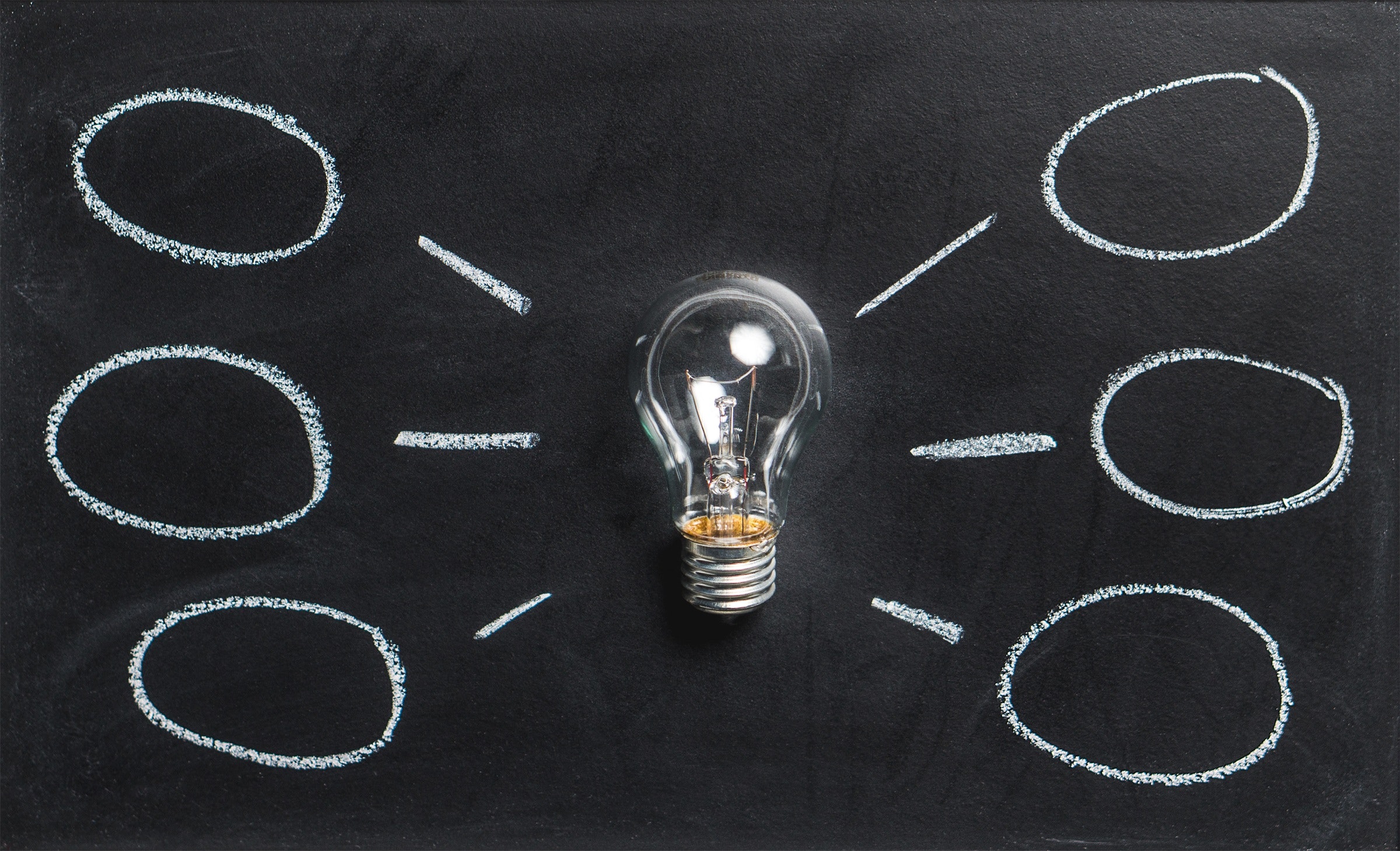 a lightbulb on a black backgrouns with chalk lines ans bubbles around it