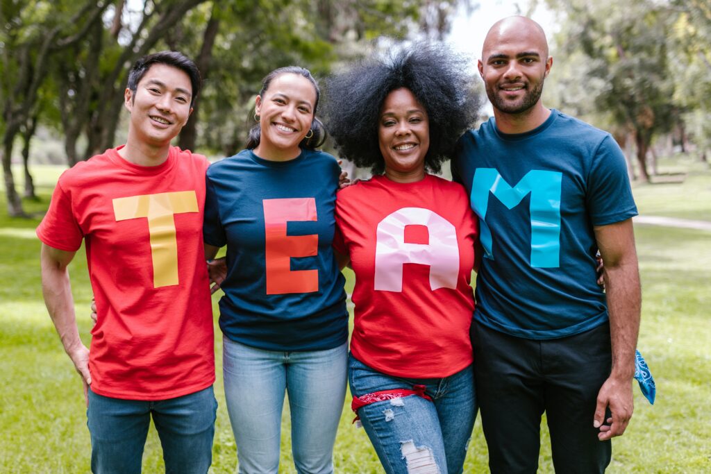 4 people of different ethnicities standing in a line with coloured tshirts spelling the word team