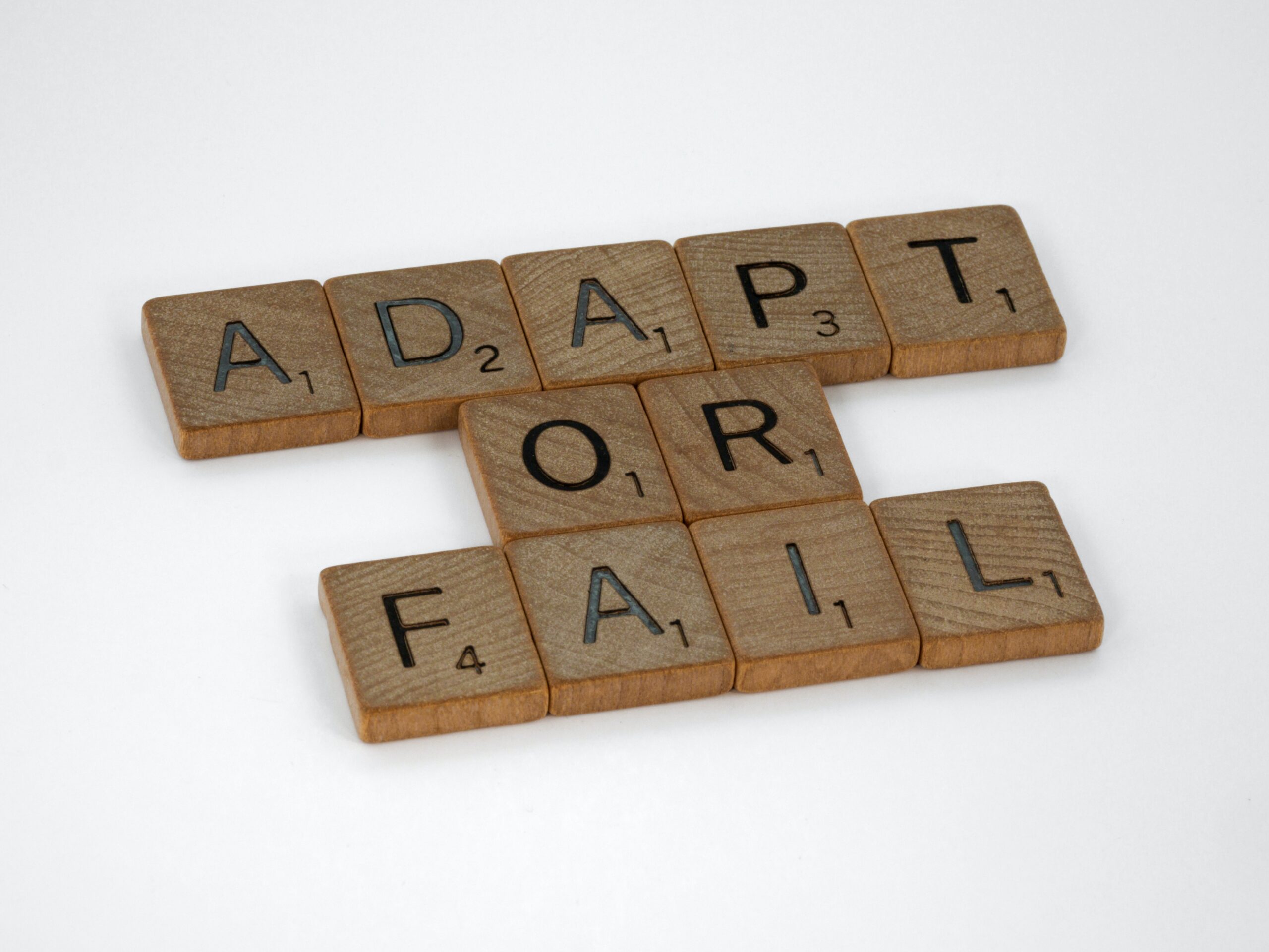 wooden tiles spelling out adapt or fail in three lines one word per line