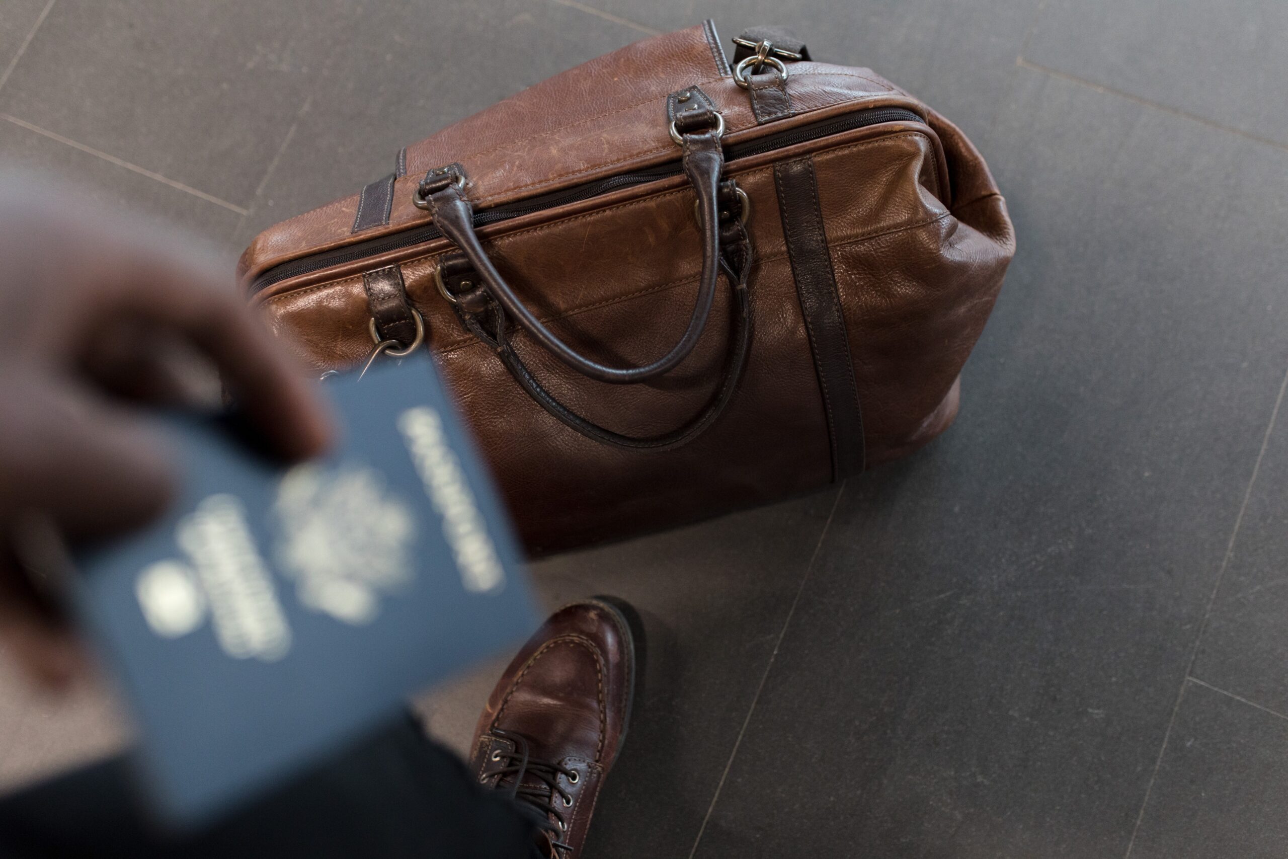 a brown holdall at a mans feet with passport in the shot