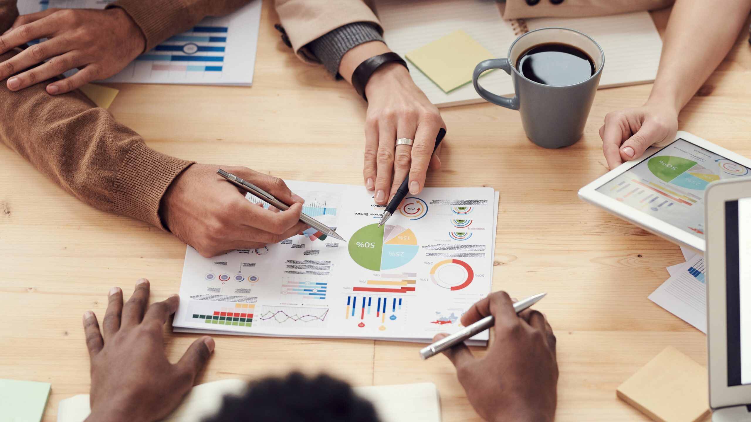 various hands over a piece of paper with pens detailing a business plan with charts