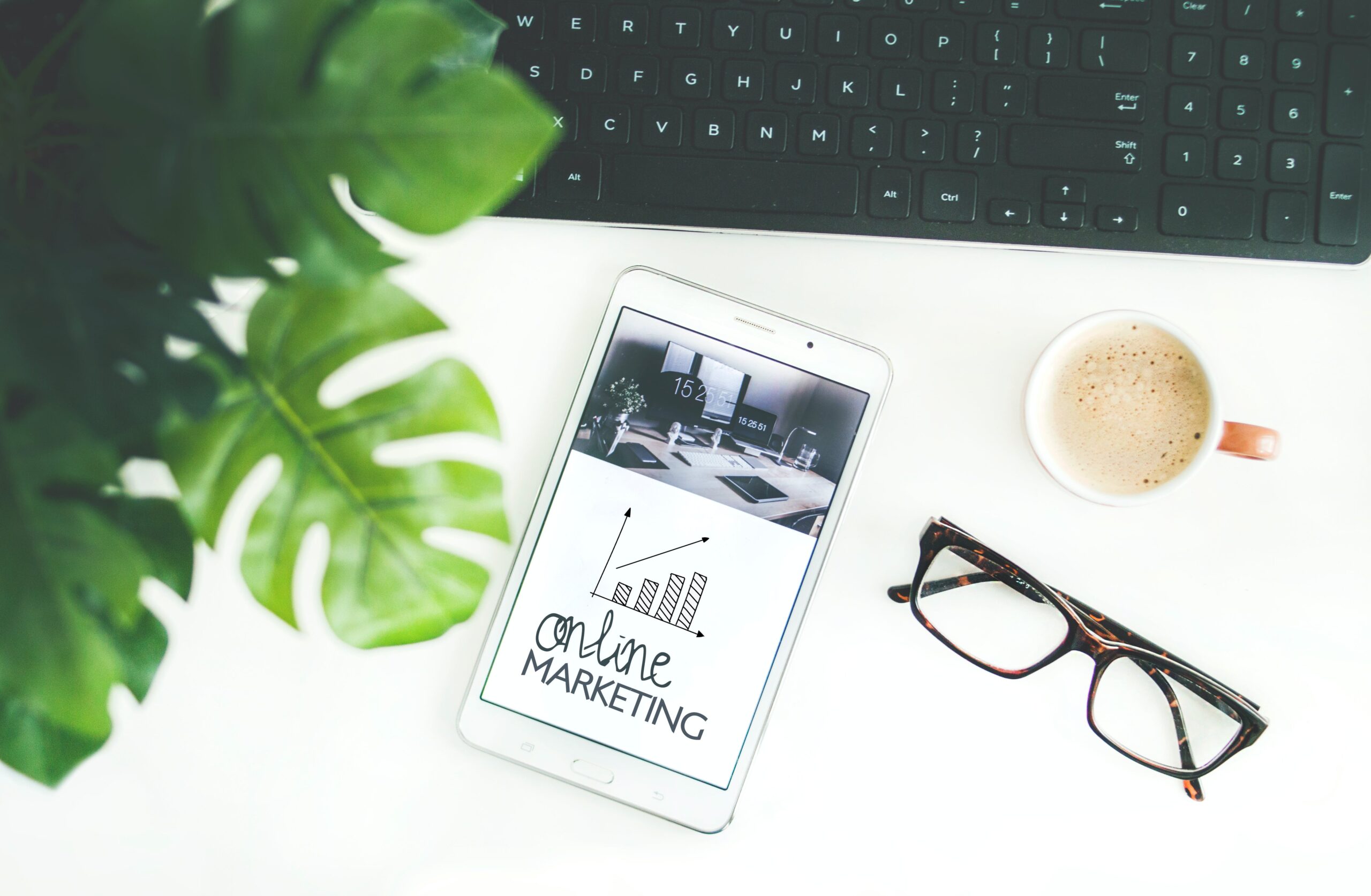 a mock up image with a mobile phone and glasses on a white table. Them obile phone says online marketing and there is a geeen leaf to the left hand side of the image
