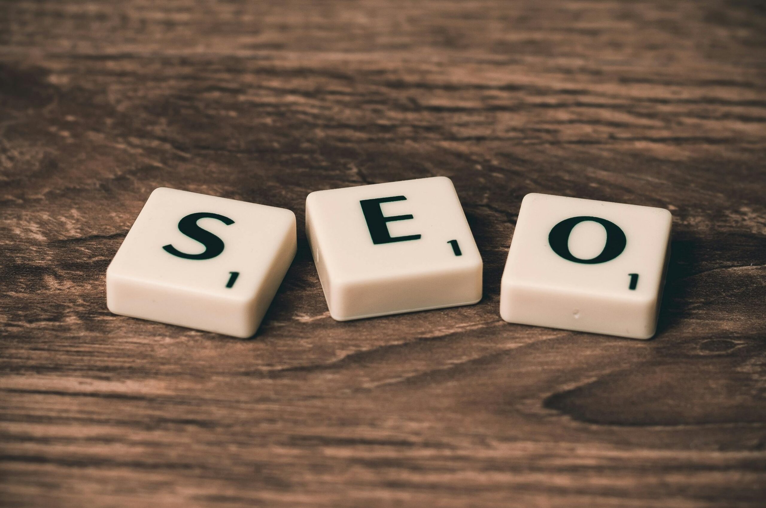 three scrabbel tiles on wooden background with the letters seo on the tiles