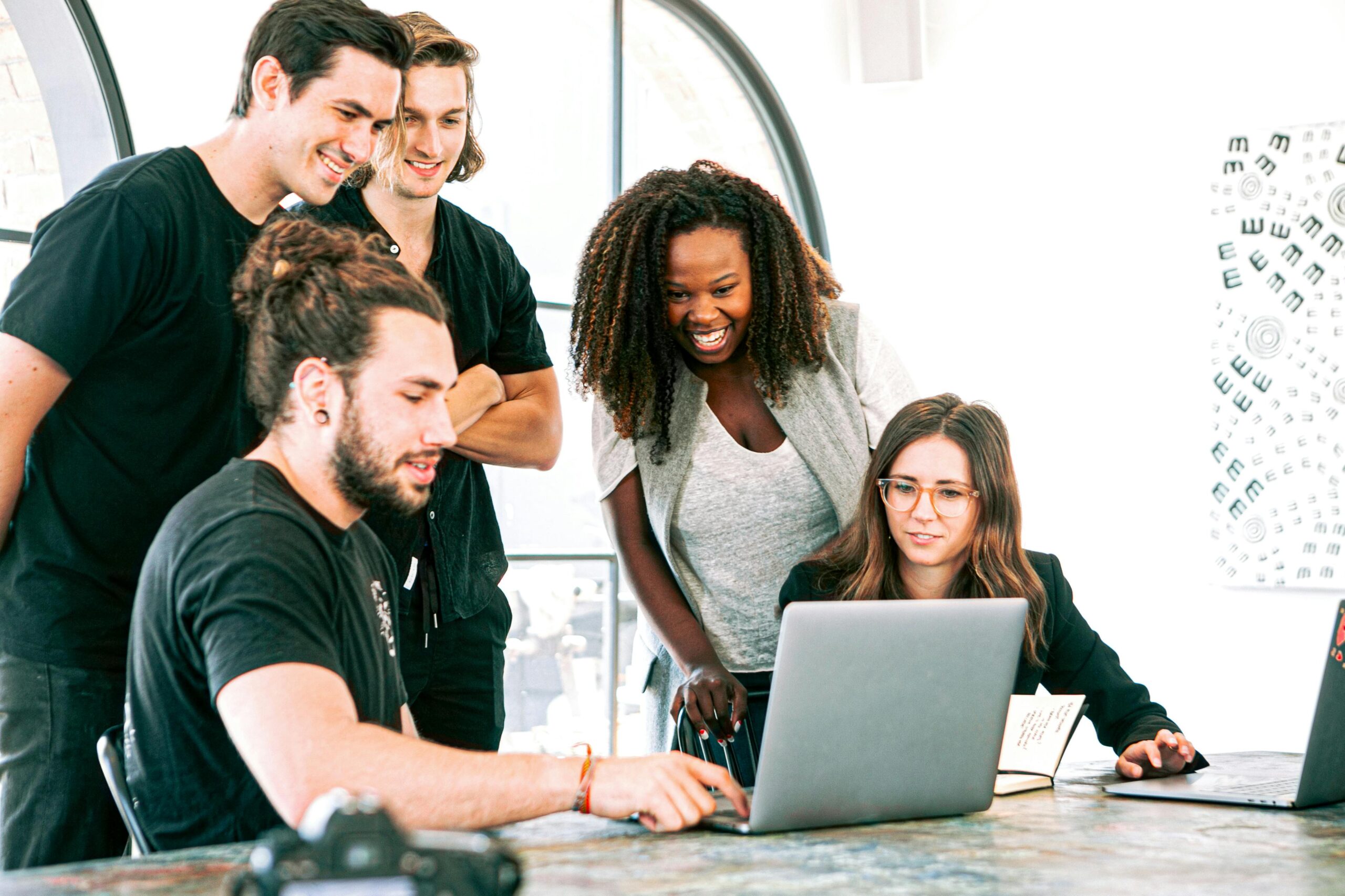 a group of people huddled aorund a laptop in an office