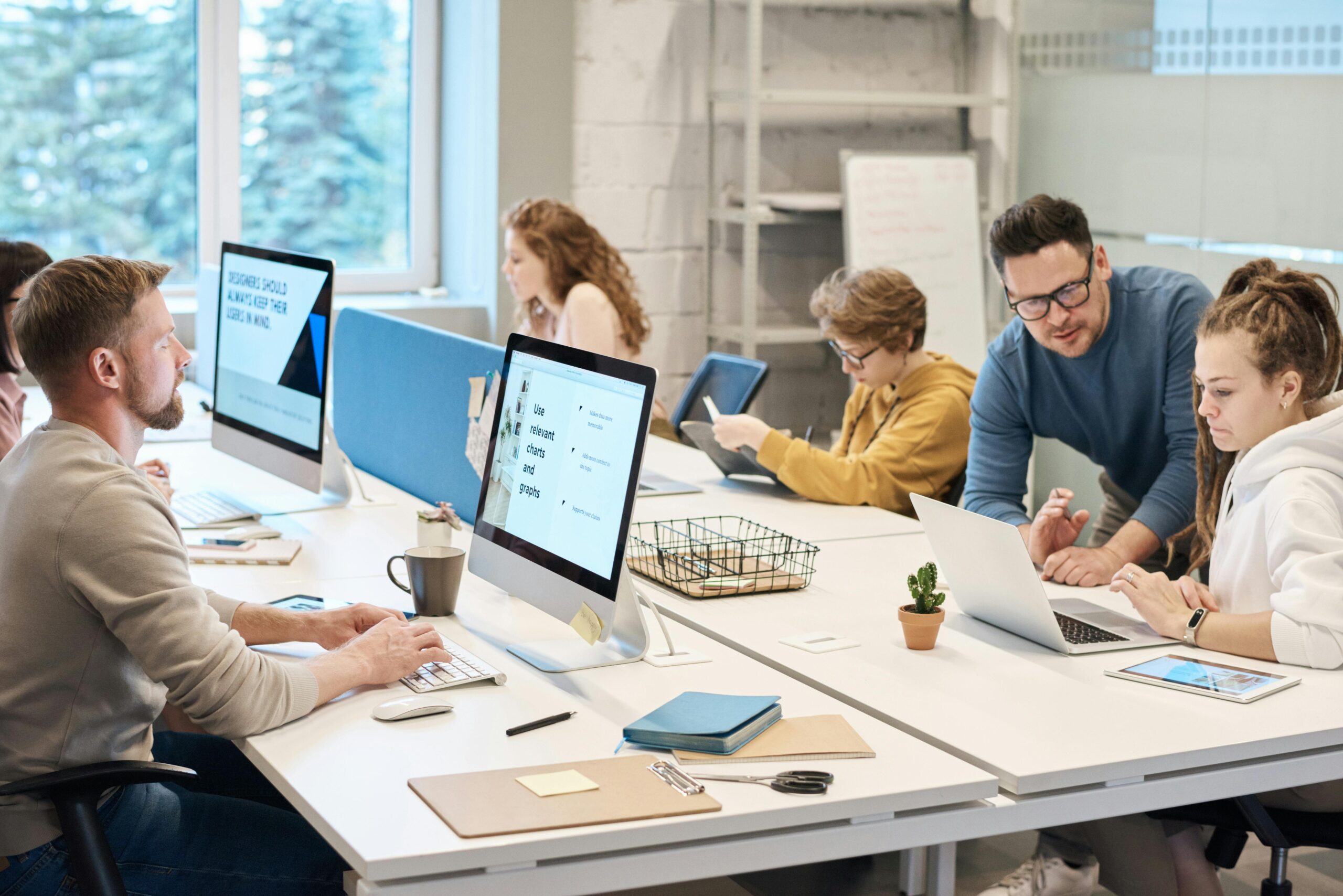 a group of employees workign aorund a shared table in fornt of PCs and laptops