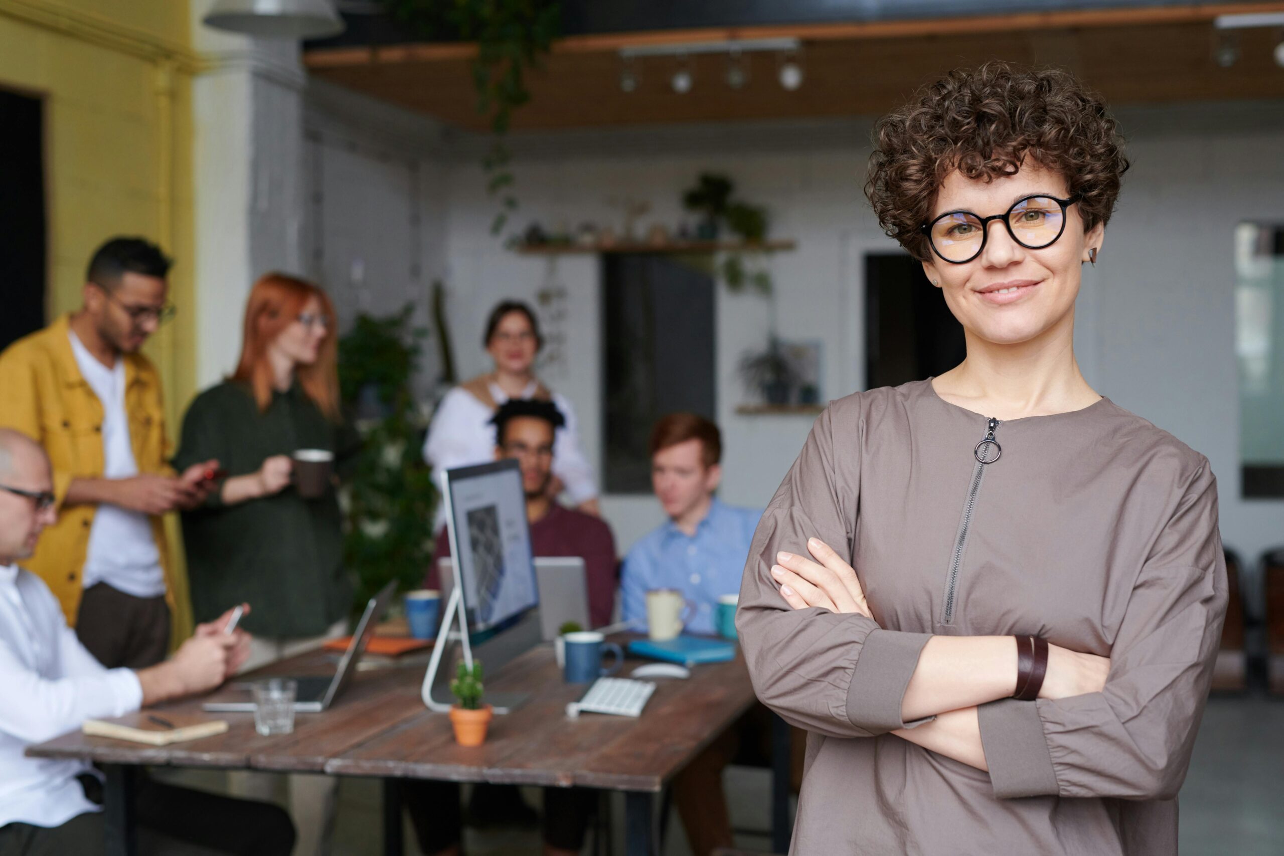 a woman in the focus on the picture with a her arms crossed and a team working away behind her