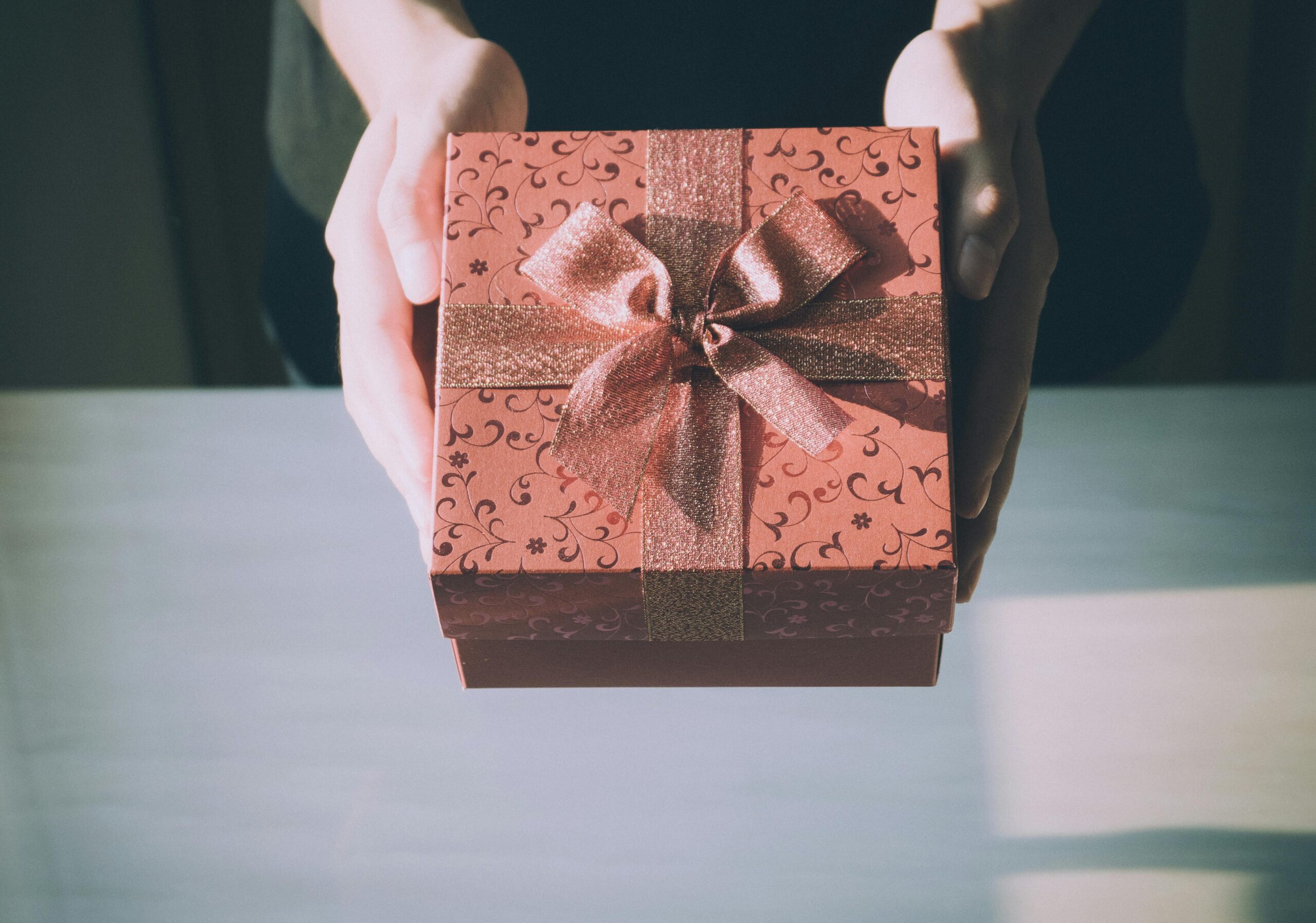a pink box with a ribbon in a bow on it being held above a desk
