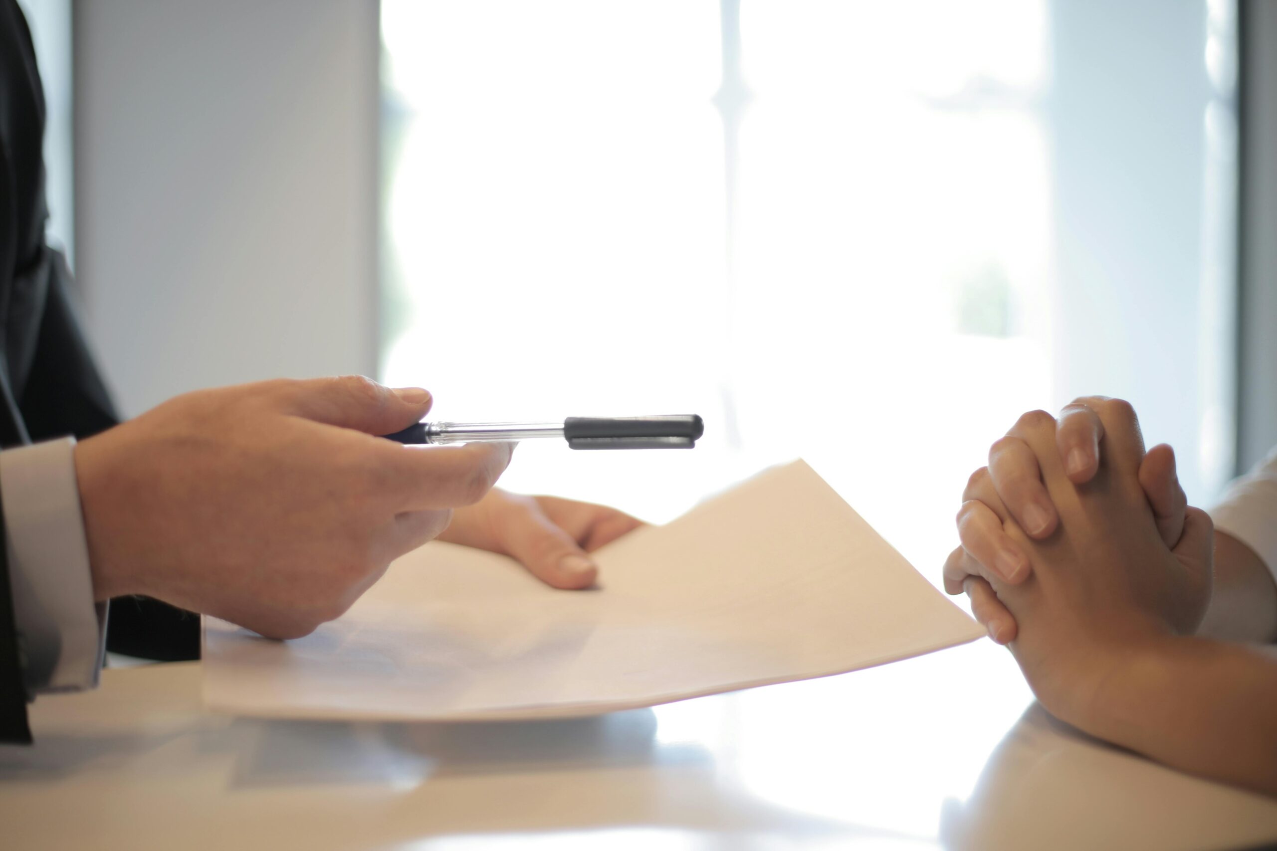 Hands exchanging contract document for signature over a desk — professional agreement in progress