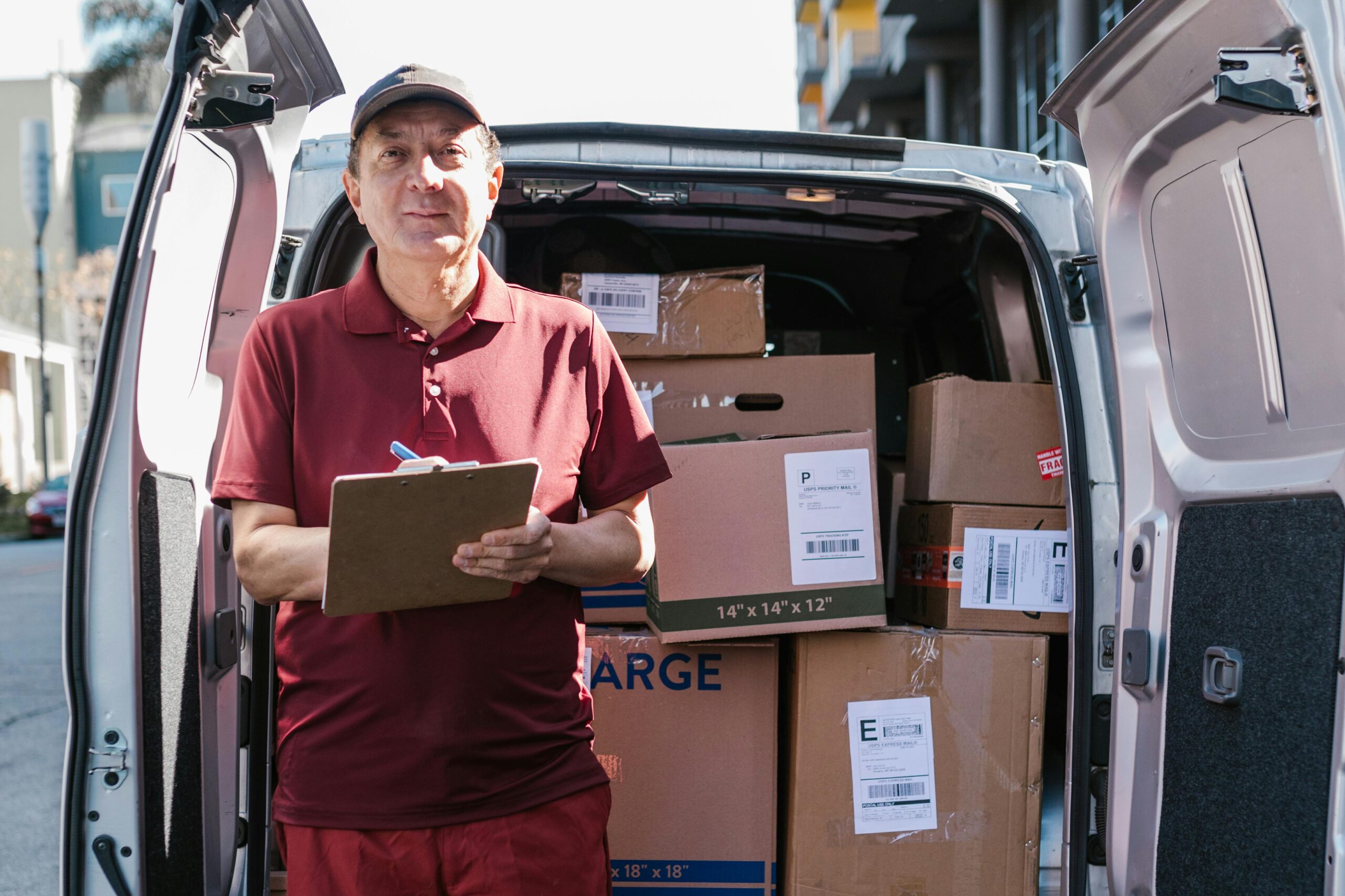 Delivery person wearing uniform holding a clipboard and scanning or checking delivery details next to a parked van.